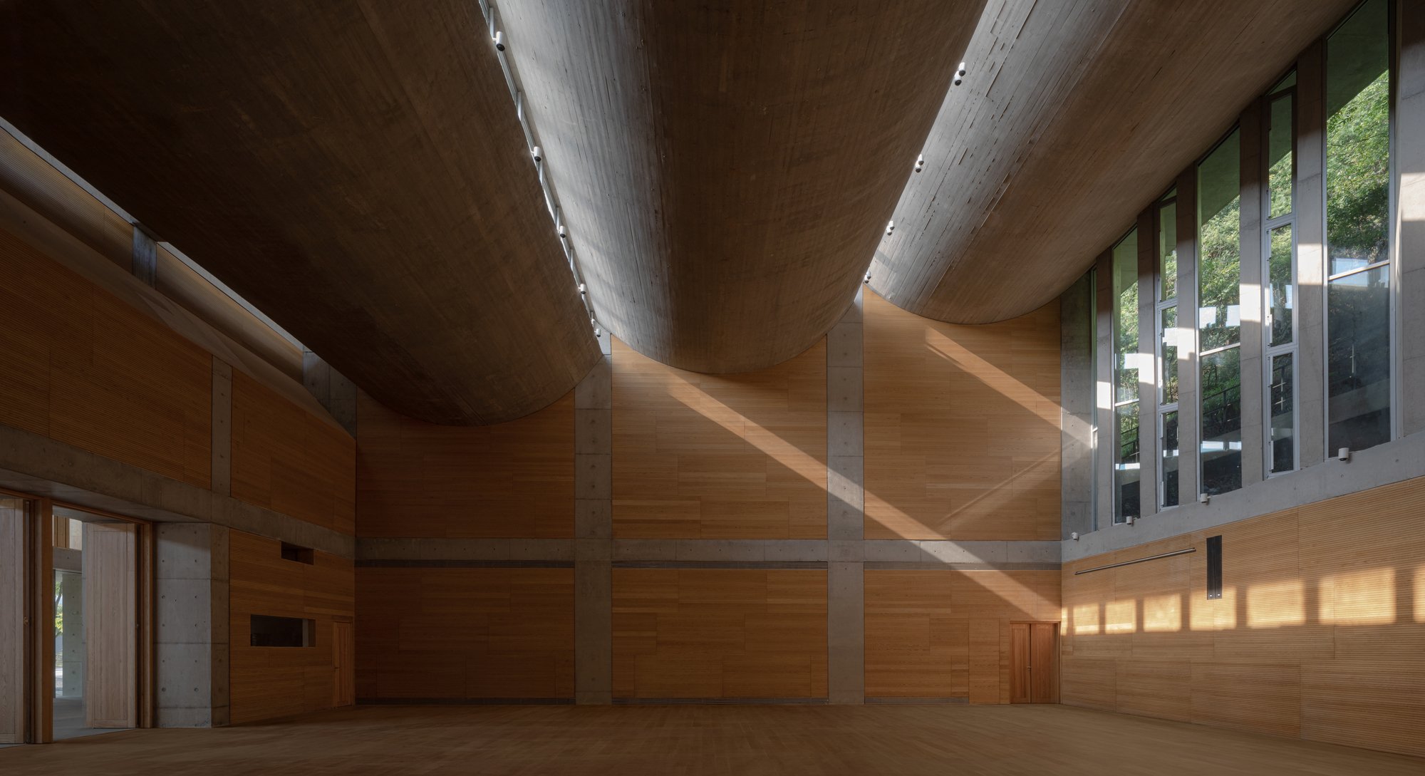 Interior of a modern building with curved wooden ceiling, large windows allowing natural light, and wood-paneled walls.