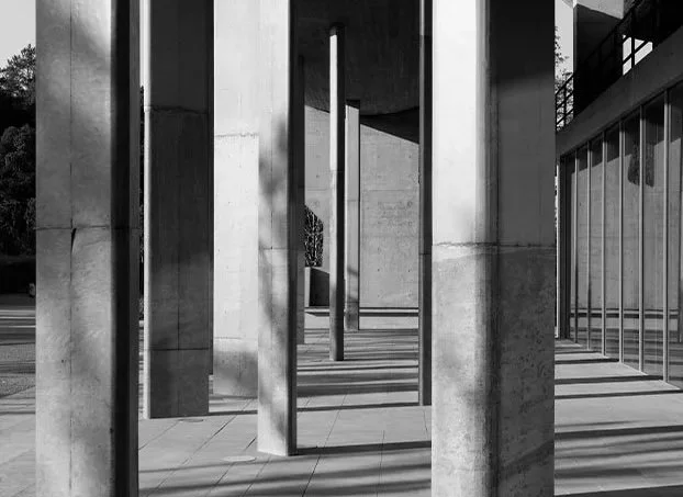 Modern architectural structure with concrete pillars and vertical metal bars, featuring shadow patterns on the ground.