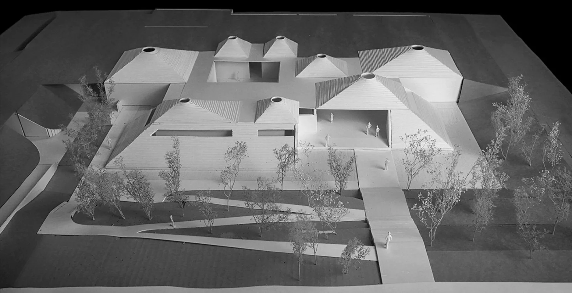 Architectural model of a modern house with multiple roofs, surrounded by trees and pathways.