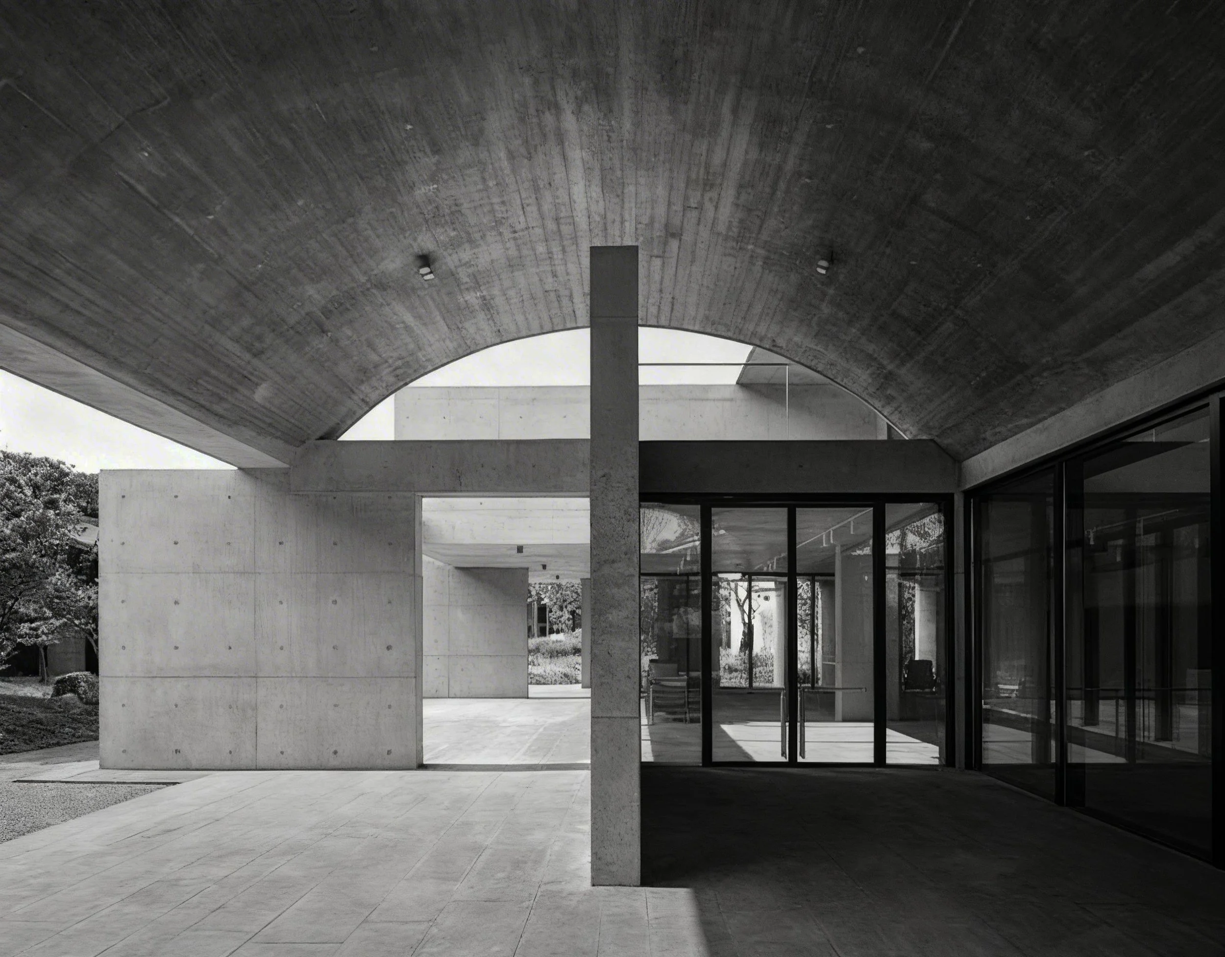 Modern building with curved concrete roof, glass walls, and outdoor patio.