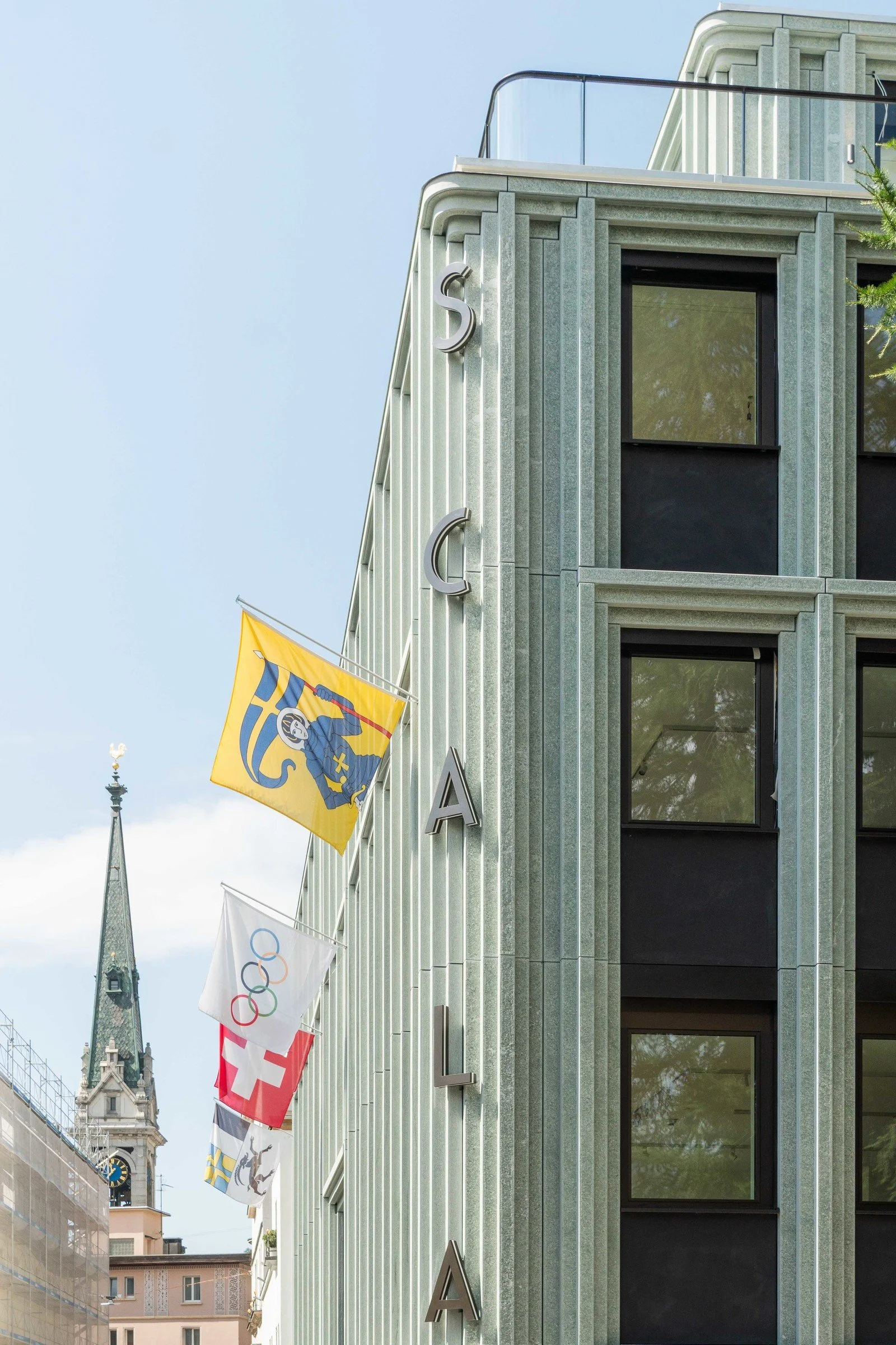 Modern building with flags, including the Swedish flag, and a church steeple in the background under a cloudy sky.