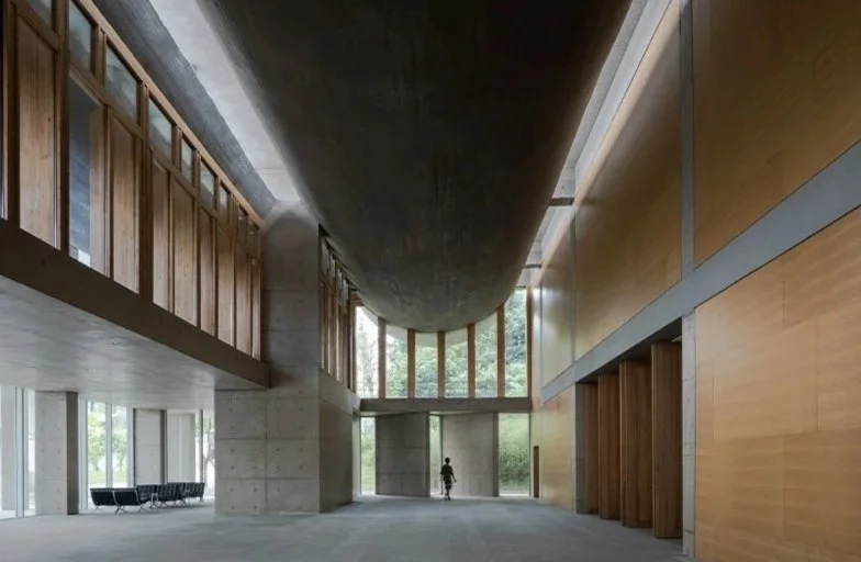 Interior of a modern building with high ceilings, large windows, and a person walking inside.