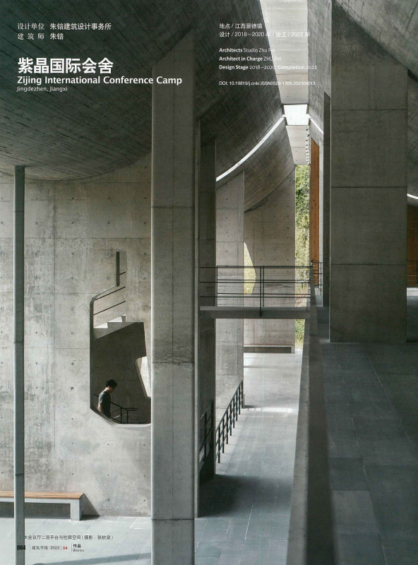 Modern architectural concrete building interior with multiple levels and walkways, a person walking down stairs, and windows showing green trees outside.