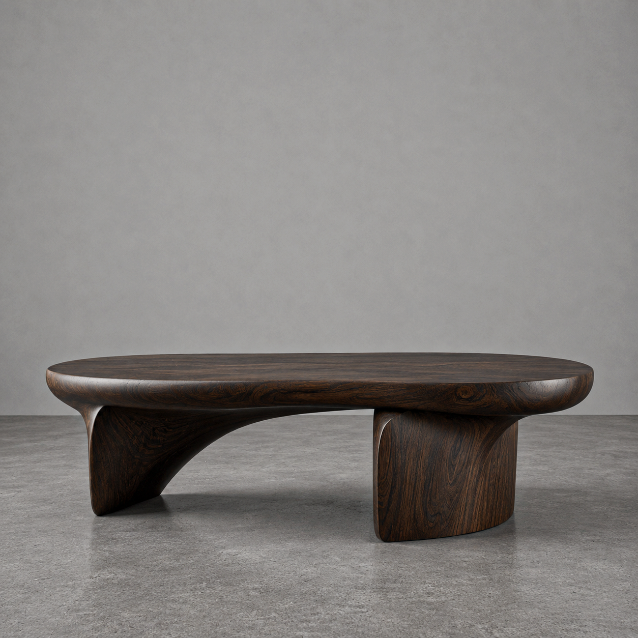 A modern wooden coffee table with a curved design, set against a grey wall and on a concrete floor.