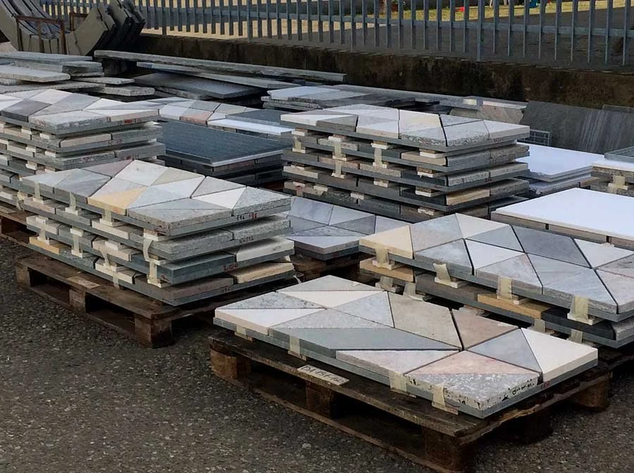 Stacks of patterned stone tiles on wooden pallets at an outdoor warehouse.