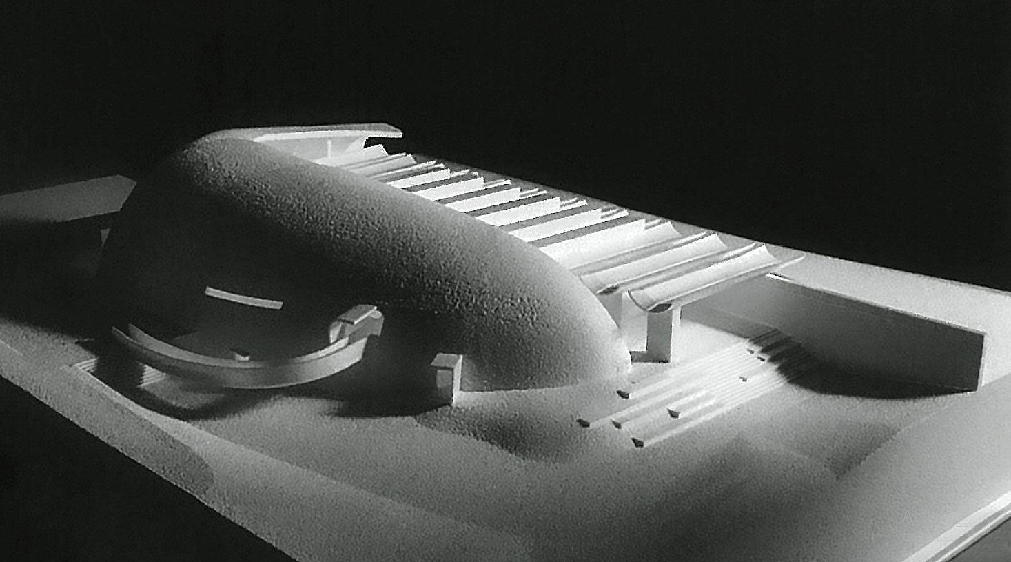 Architectural model of a sports stadium with an oval roof and surrounding seating areas.