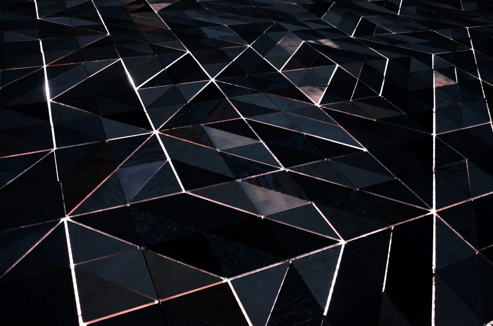 A geometric pattern of black triangular tiles with white lines outlining each tile, creating a sparkling, mosaic-like surface.