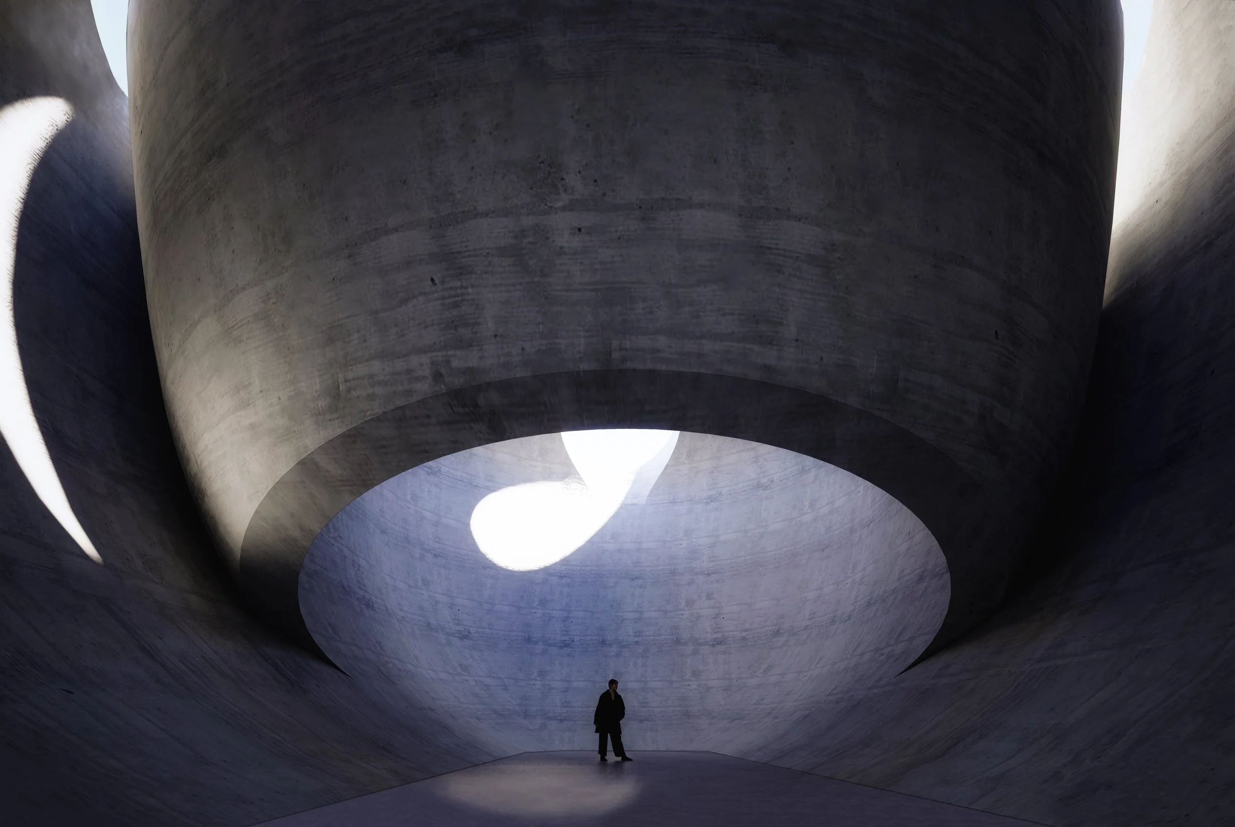 Person standing inside a large concrete tunnel with smooth, curved walls and a circular opening at the top illuminated by natural light.