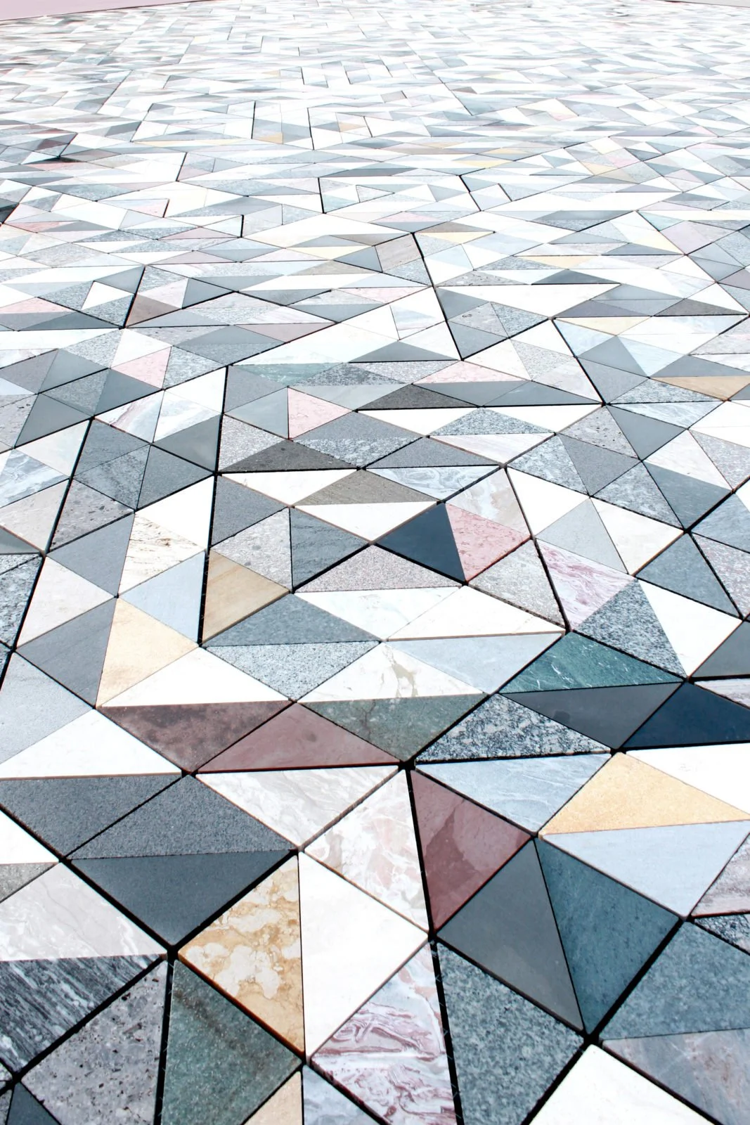 Colorful geometric tile floor with various shades of gray, white, beige, pink, and green arranged in triangles and other polygon shapes.