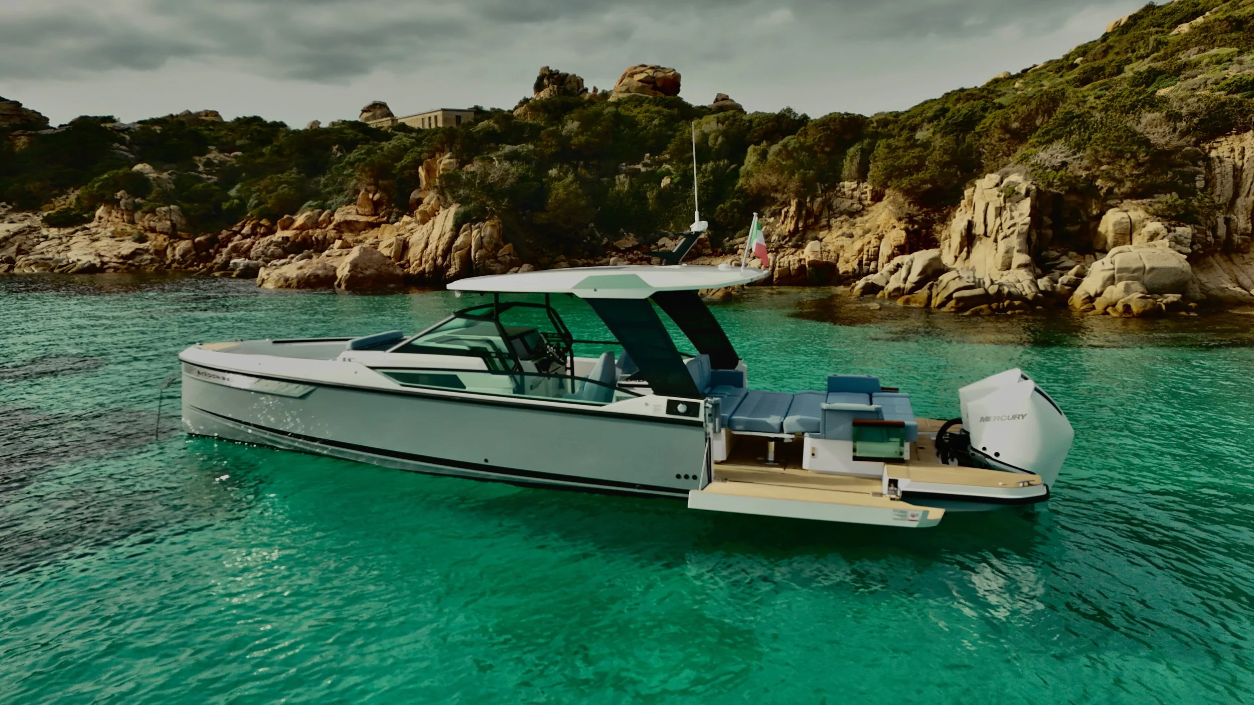 Immagine di una barca a motore moderna sulla acque verdi di un mare calmo, con rocce e vegetazione sullo sfondo ettirico e nuvole nel cielo.