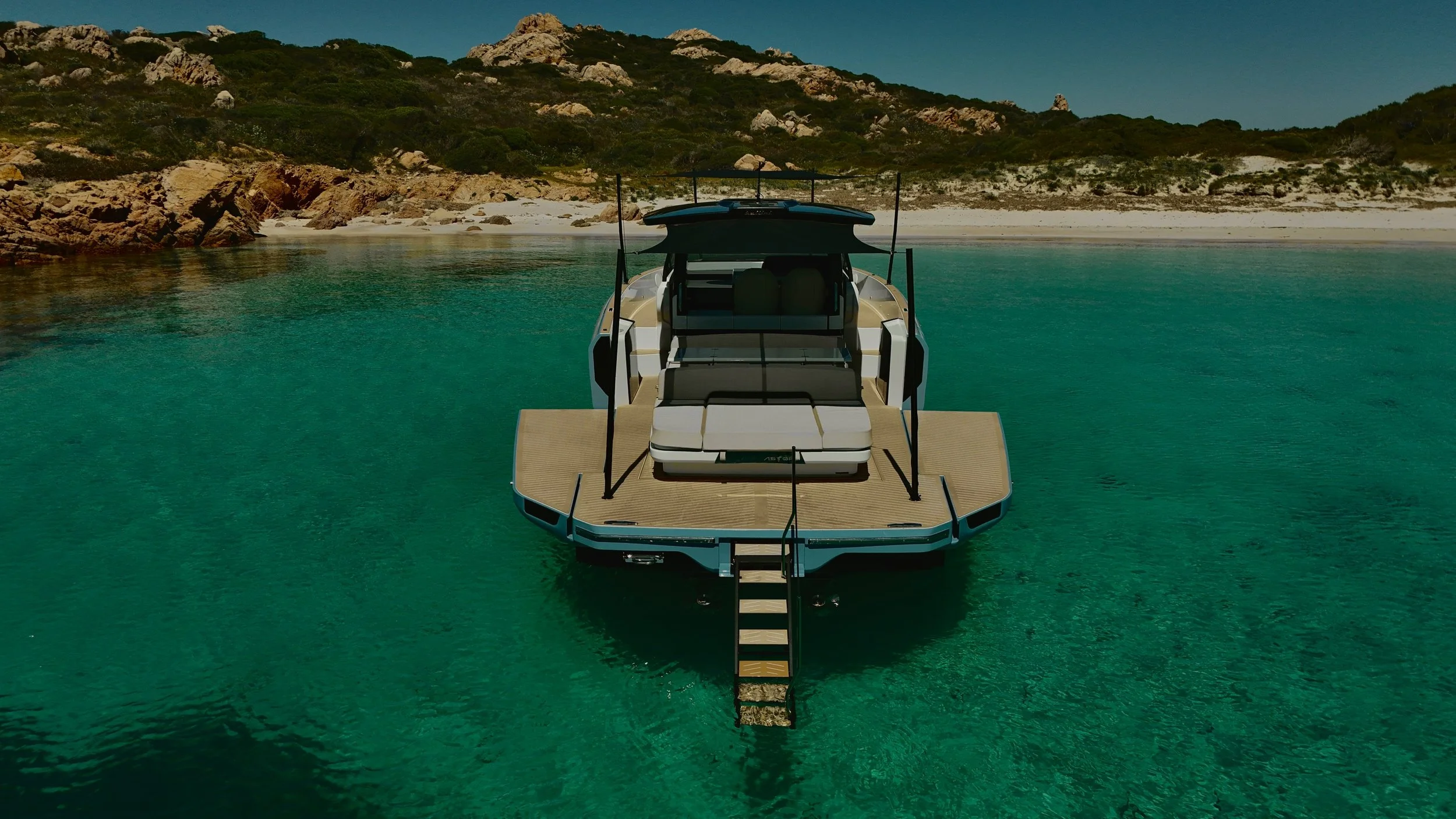 Barca a vela in acqua vicino a una spiaggia con rocce e collina verde sullo sfondo.