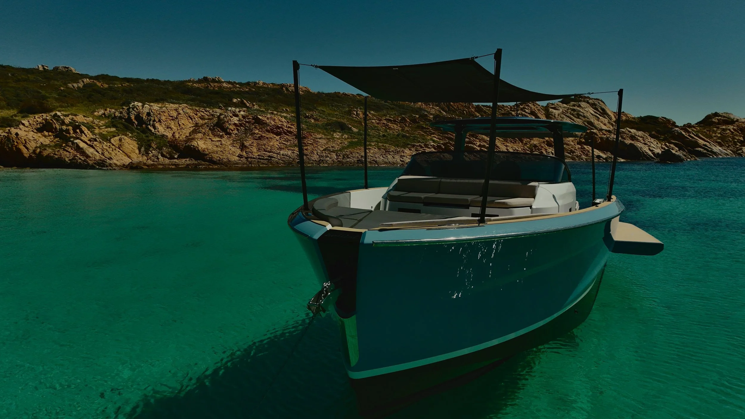 Barca a motore ormeggiata in acque turchesi con una spiaggia e colline rocciose sullo sfondo