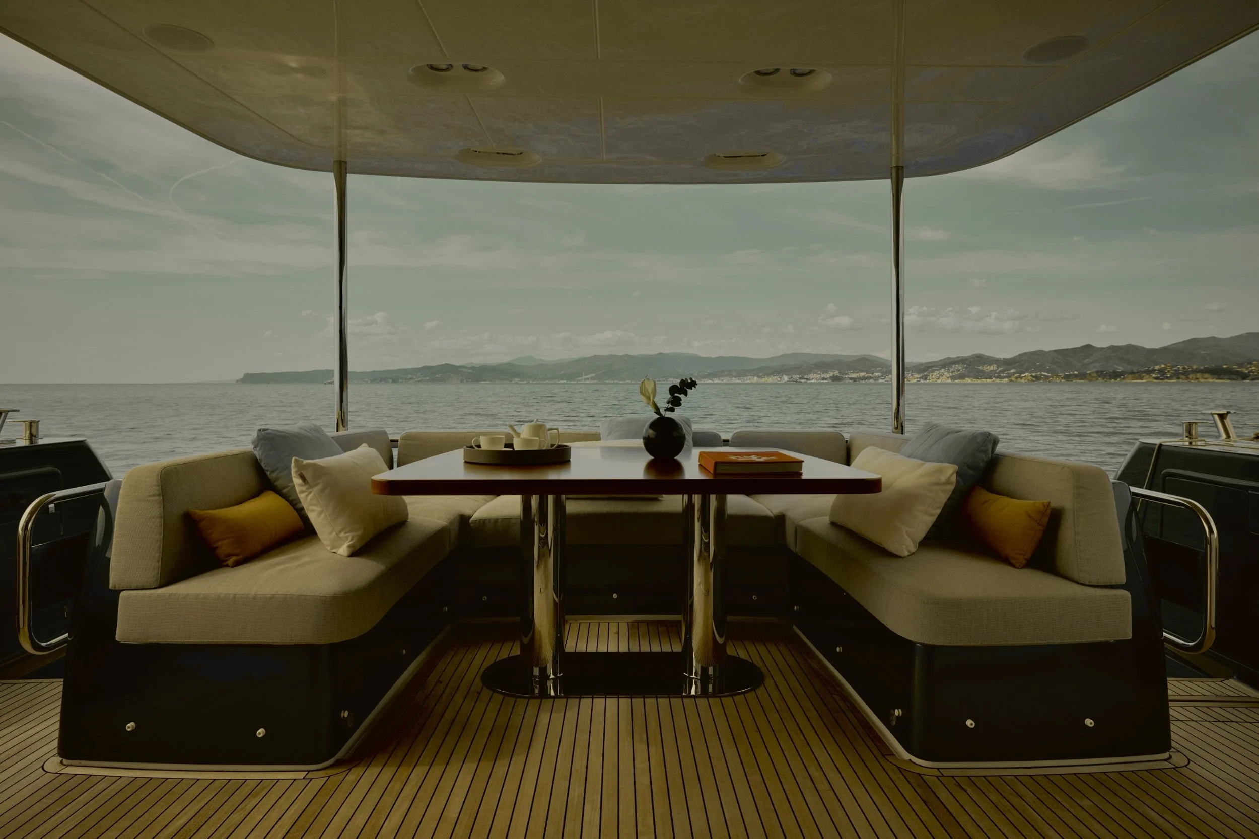 Zona relax su una barca con vista sul mare e le montagne sullo sfondo, arredamento confortevole con divani, un tavolo con una pianta e tazze.