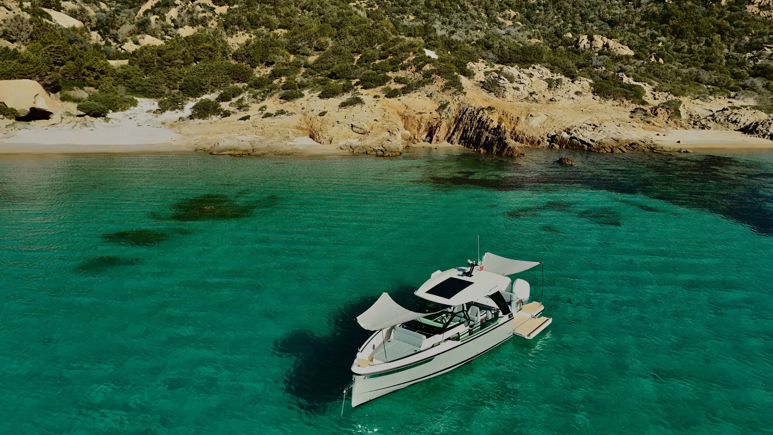 Immagine di uno yacht bianco attraccato in acque verdi, con scogliera e vegetazione sullo sfondo.