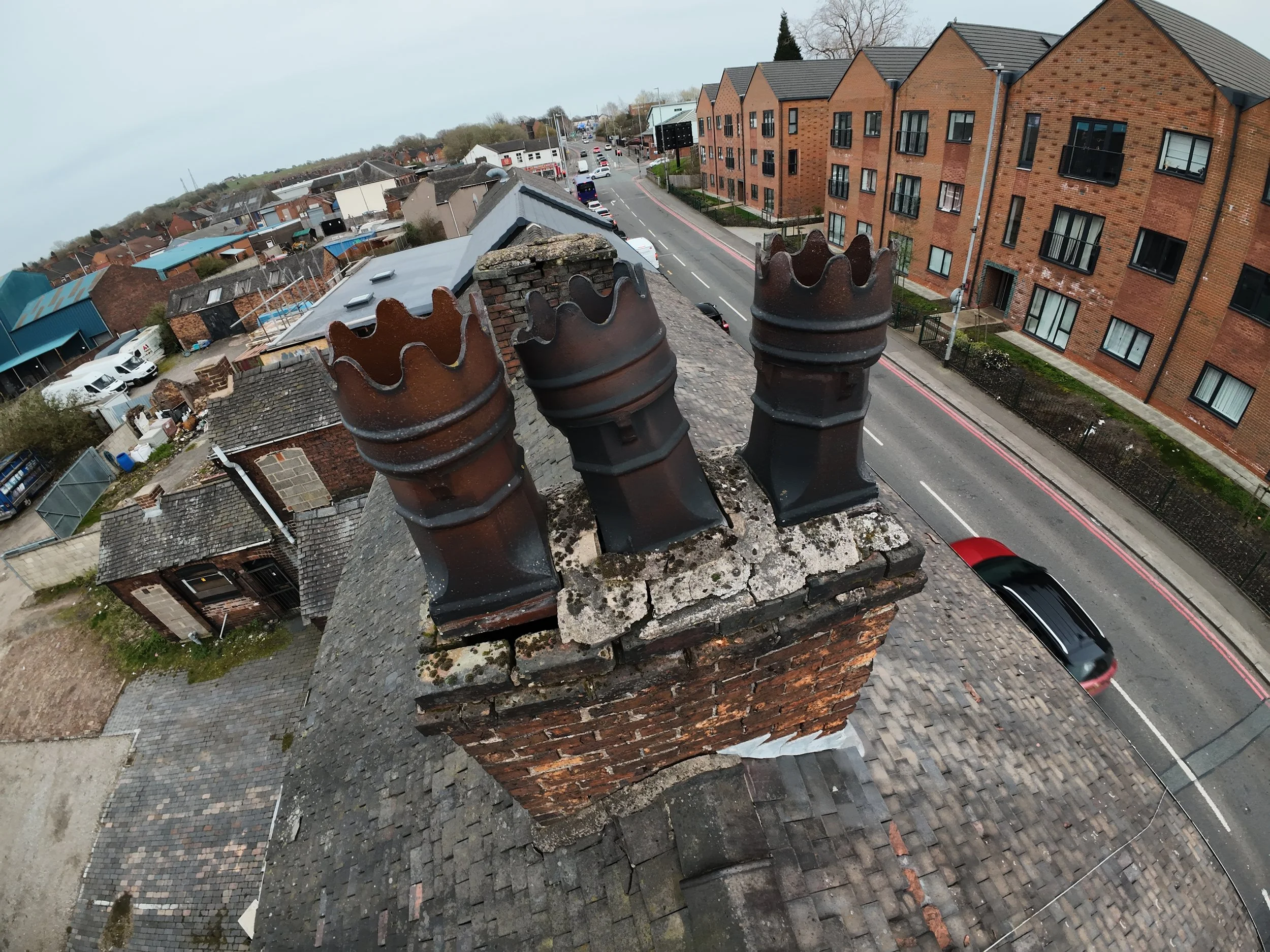 Deteriorated chimney stack with loose clay pots and missing mortar captured during a drone roof inspection.