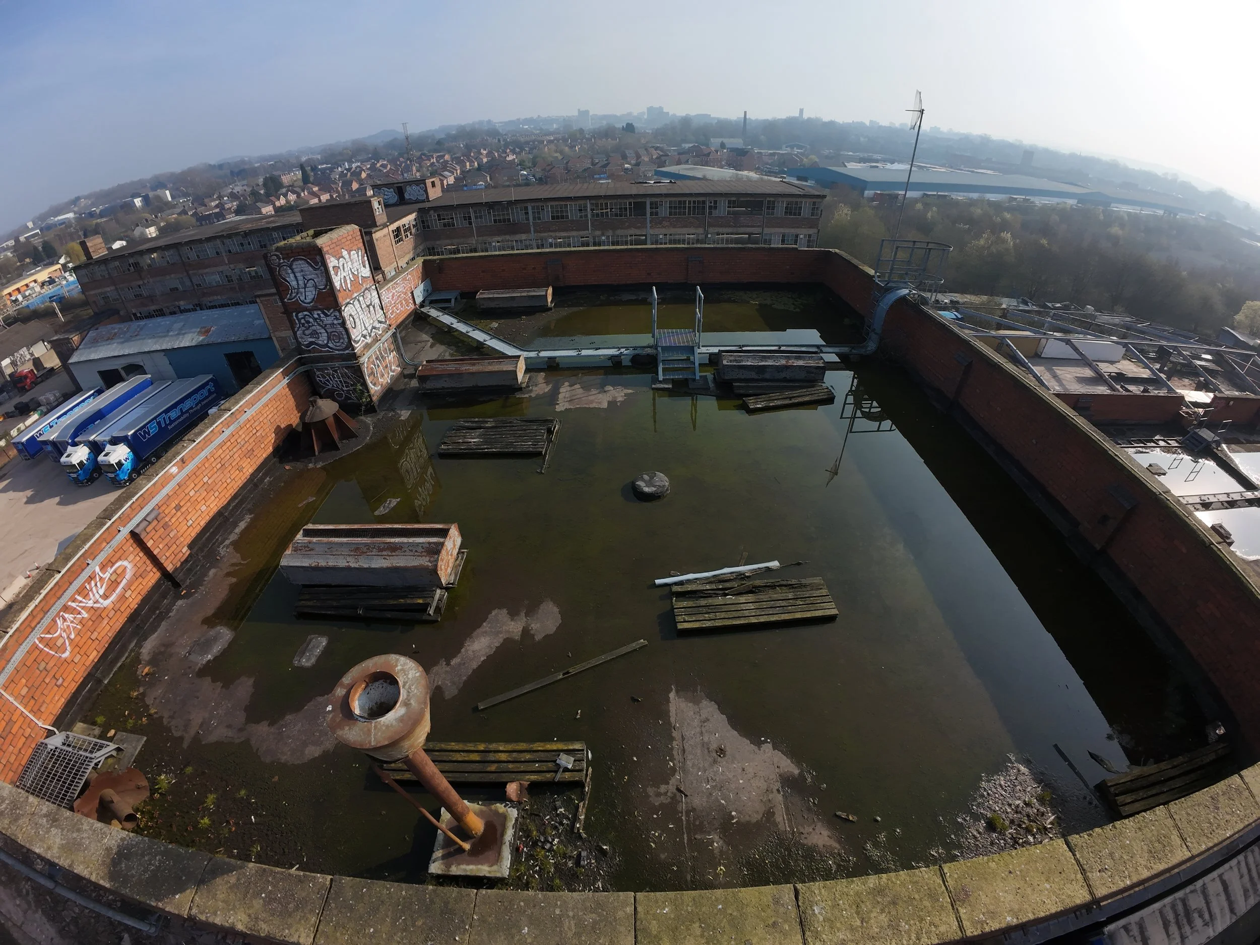 Drone photo of a derelict flat roof covered in standing water, broken wooden boards, debris, and deteriorating brickwork, showing severe drainage issues and structural neglect.