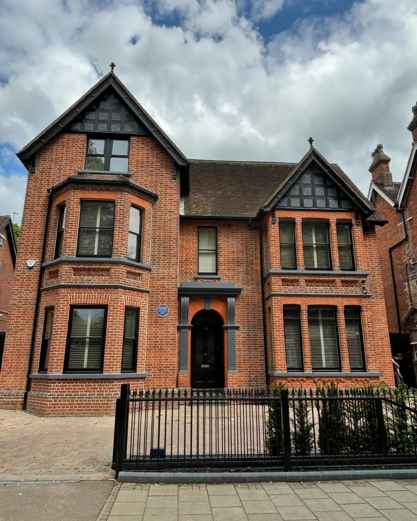 A red brick Victorian-style house with pointed gable roofs, multiple windows with black frames and white blinds and a black front door, beautifully restored by the Bedford Victorian Restoration team.