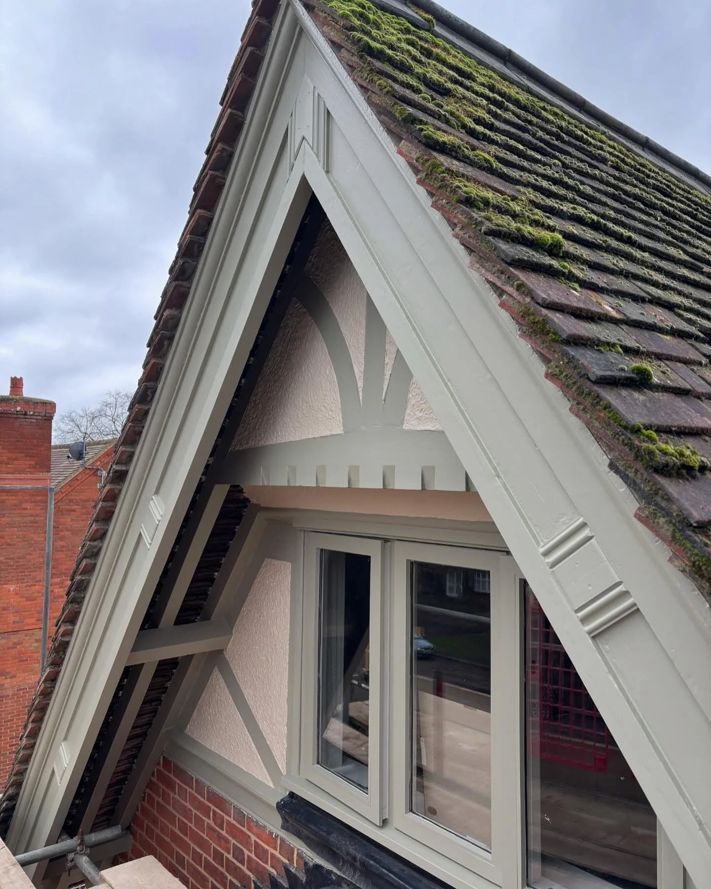 Close-up view of a Victorian house's attic window with a white frame, set in a dormer with a brick exterior,  restored by the Bedford Victorian Restoration team.