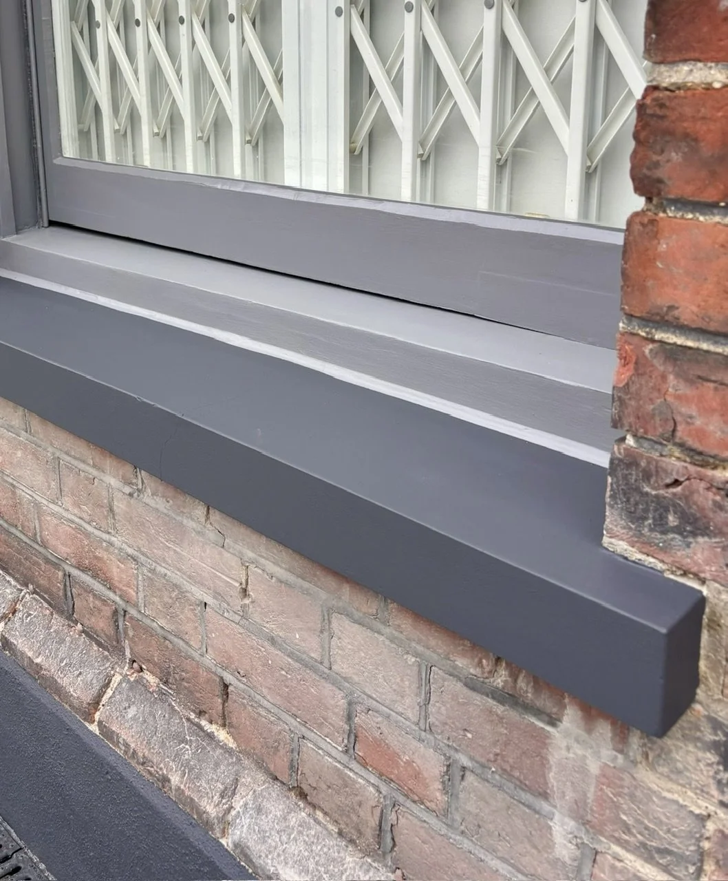 A close-up of a brick Victorian building exterior showing a window with a window sill painted in gray, pre-restoration by the Bedford Victorian Restoration team.