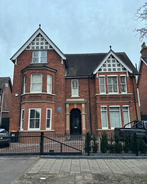 A large, historic brick house with Victorian architectural features, including bay windows and gabled roof.