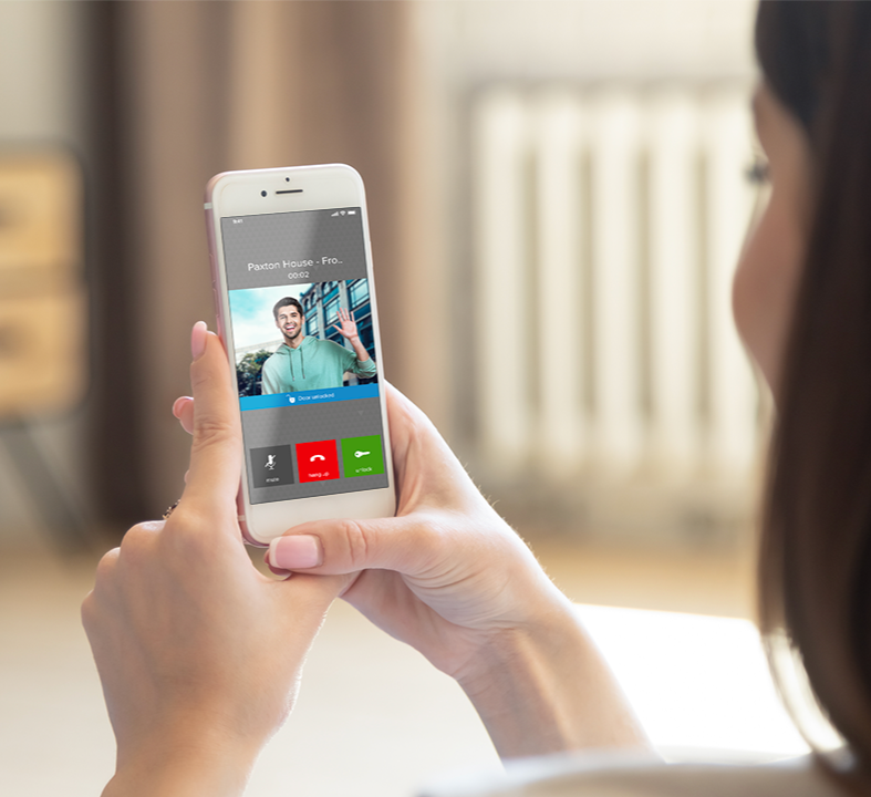 A woman holding a smartphone during a video call with a young man waving on the screen.