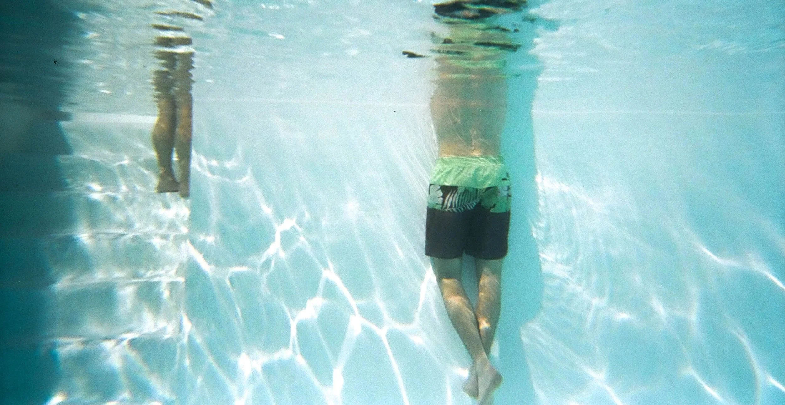 Due persone che nuotano sott'acqua in una piscina, una di fronte all'altra