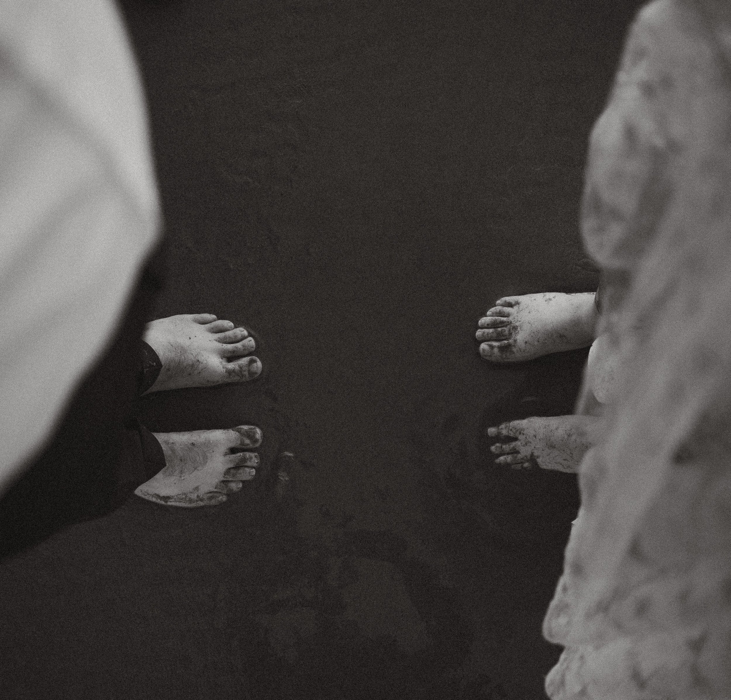 Black and white photo of four people barefoot with dirty feet, standing on a dark wooden floor.