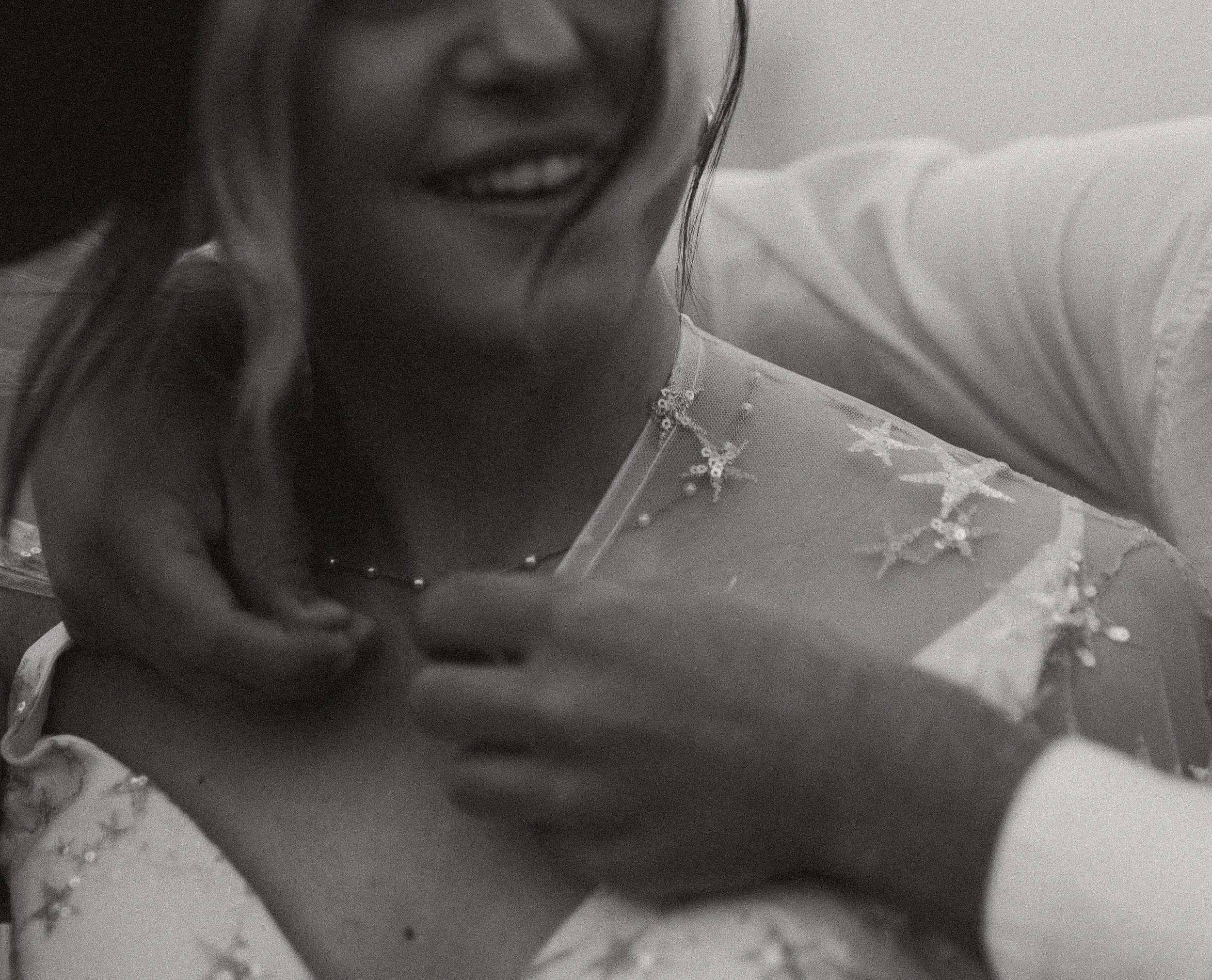 A woman smiling, touching her face and shoulder, wearing a dress with star pattern and a necklace.