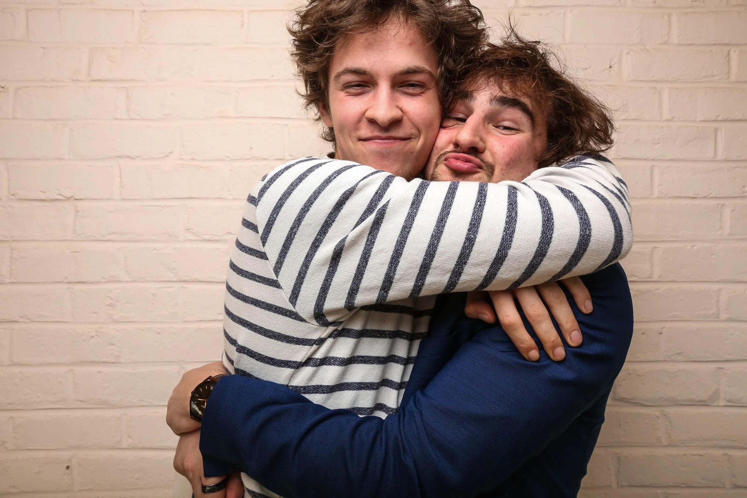 Deux hommes s'embrassent en souriant devant un mur en briques blanches, photo pris avec notre photo booth.