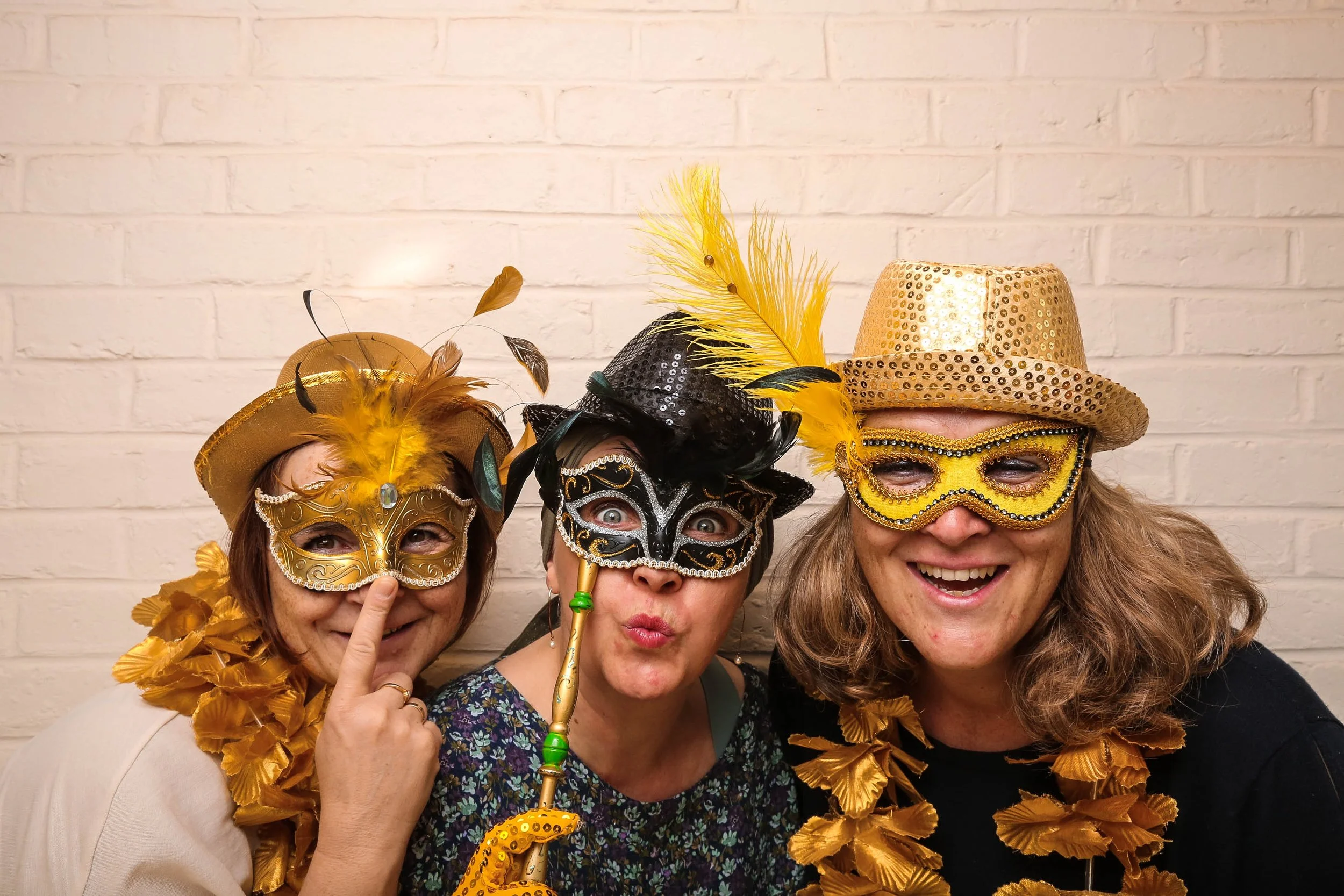 Trois femmes portant des masques, chapeaux et colliers colorés lors d'une fête costumée, souriant, photo pris avec notre photo booth.
