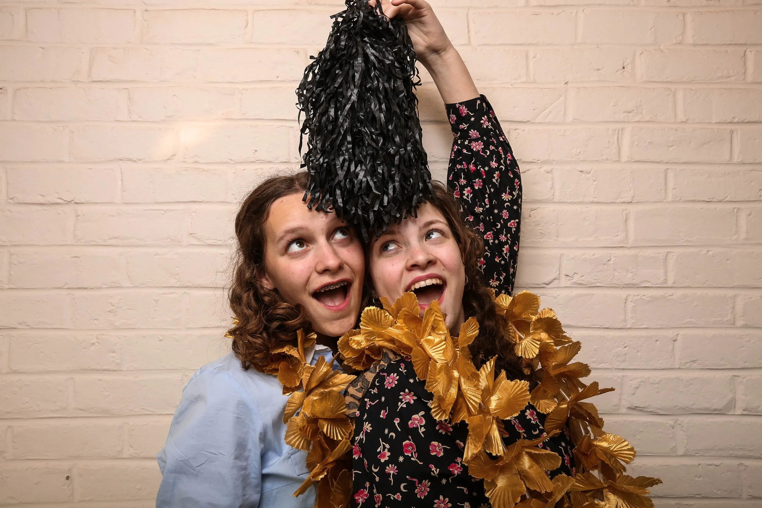 Deux jeunes femmes souriantes avec des décorations dorées autour du cou, une qui tient un objet noir en banderole au-dessus de sa tête, photo pris avec notre photo booth.