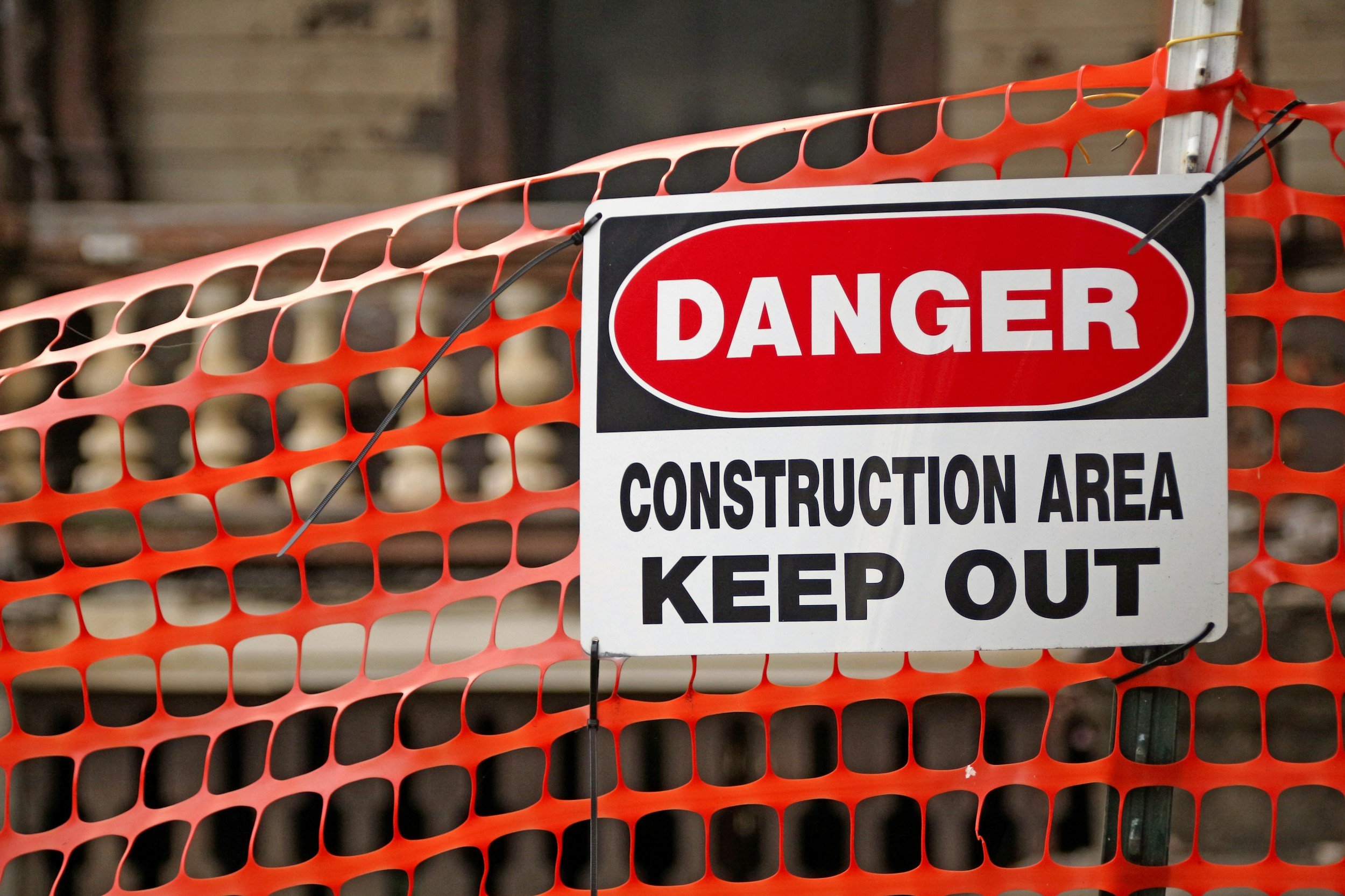 Warning sign on orange construction fencing that says 'Danger Construction Area Keep Out'.