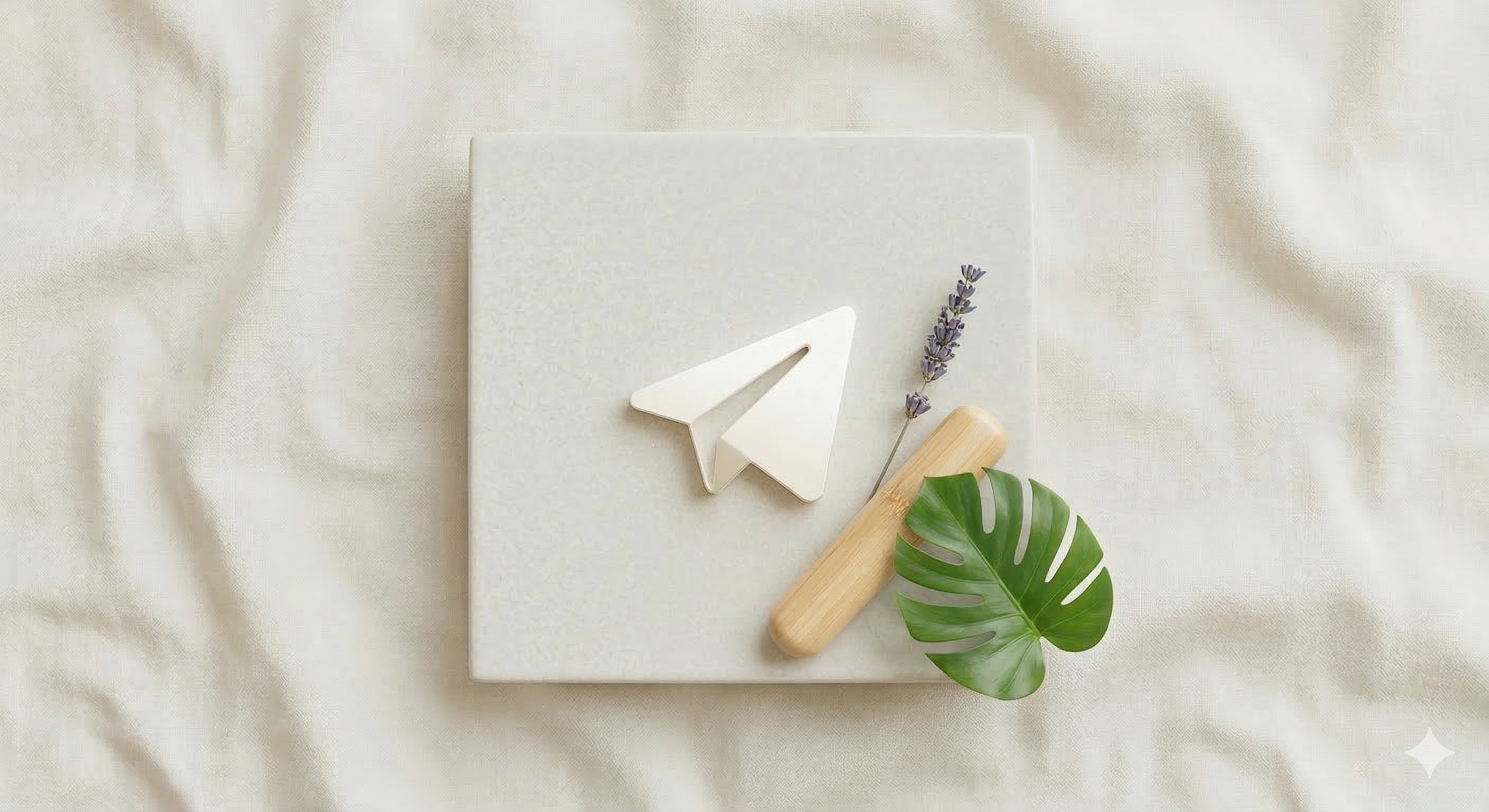Un cuaderno blanco sobre tela beige, decorado con una figura de papel en forma de avión, una ramita de lavanda, un rodillo de madera y una hoja grande de monstera.