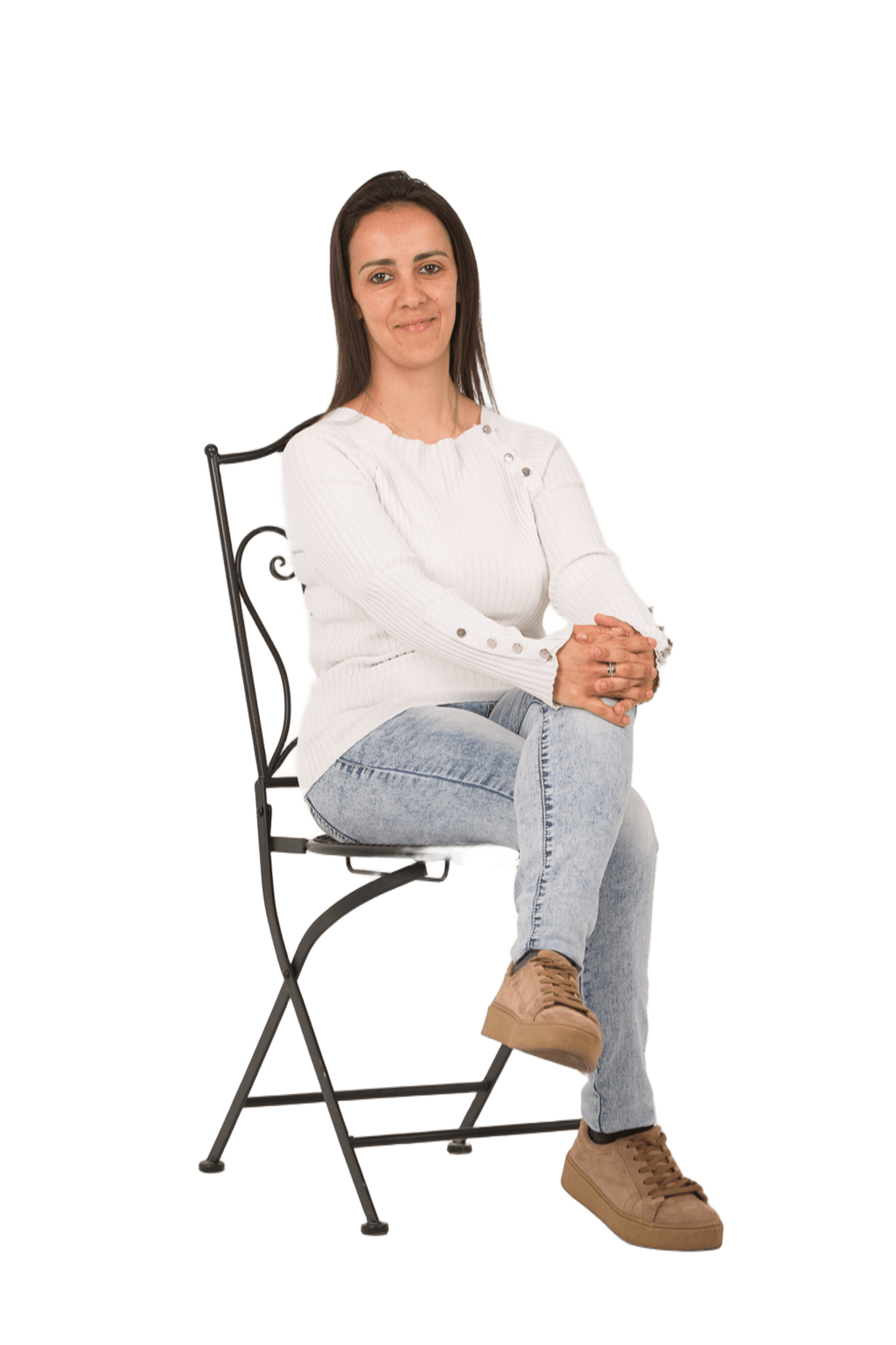 Mujer sentada en una silla metálica de espaldas con los brazos cruzados, vestida con suéter blanco y pantalones vaqueros, estilo casual, expresión relajada.
