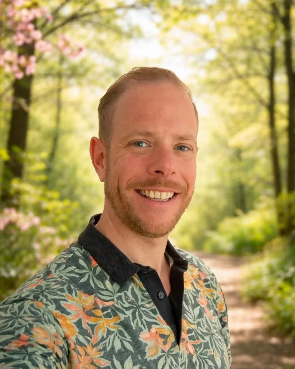 Een man die lacht terwijl hij in een bos wandelt tijdens zonnig weer.