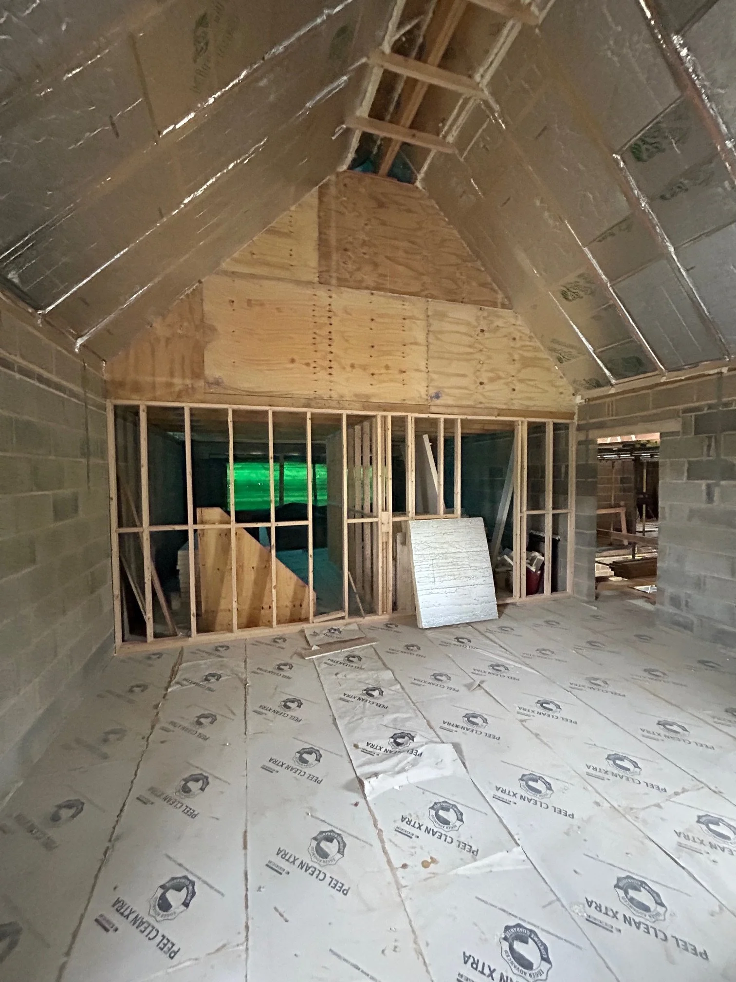 Construction site of a small room with unfinished walls, insulation, and wooden framing for a chimney or stove vent. Protective floor covering in place.