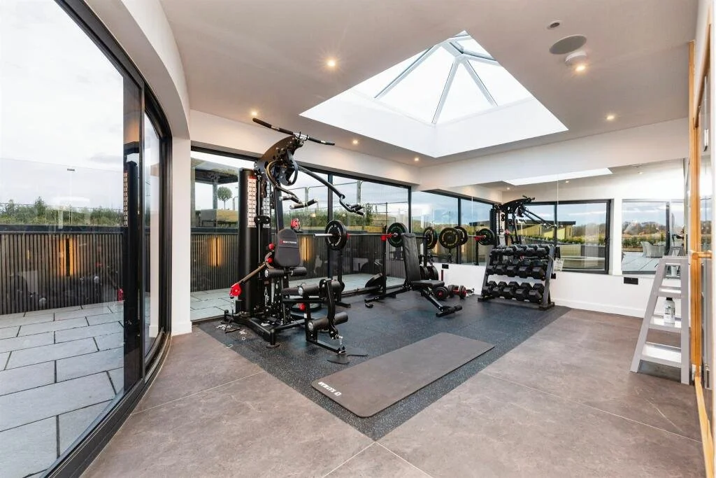 Home gym with weightlifting equipment and large windows showing outdoor view.