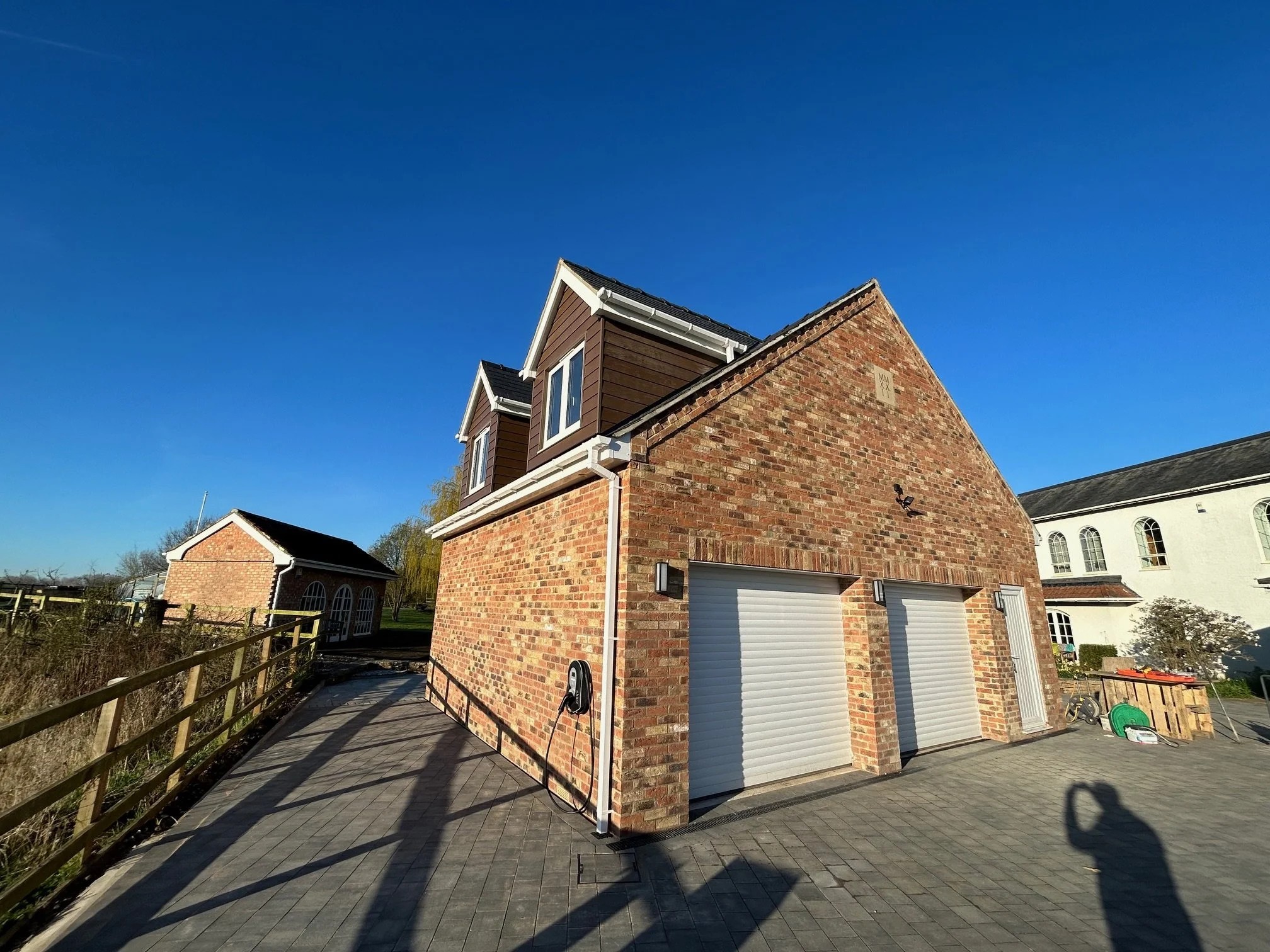 A brick garage with two white roll-up doors and a small white side door, situated on a paved driveway under a clear blue sky.