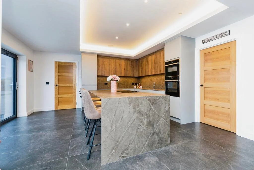 Modern kitchen with wooden cabinets, a stone island with seating, black tiled flooring, and a sliding glass door.