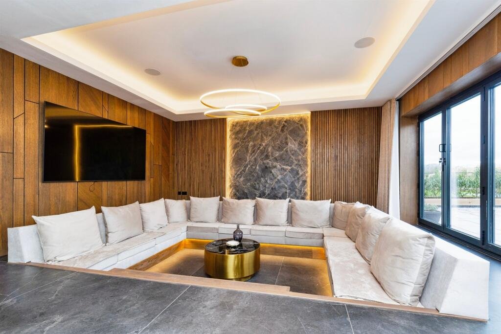 Modern living room with a large white sectional sofa, black flat-screen TV, wood-paneled walls, a marble accent wall, and a window with curtains.