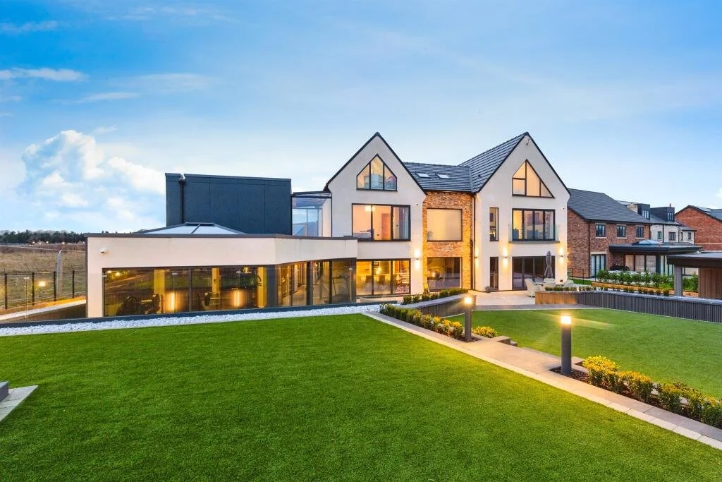 Modern residential house with large glass windows, brick accents, and a well-maintained lawn with pathway lights.