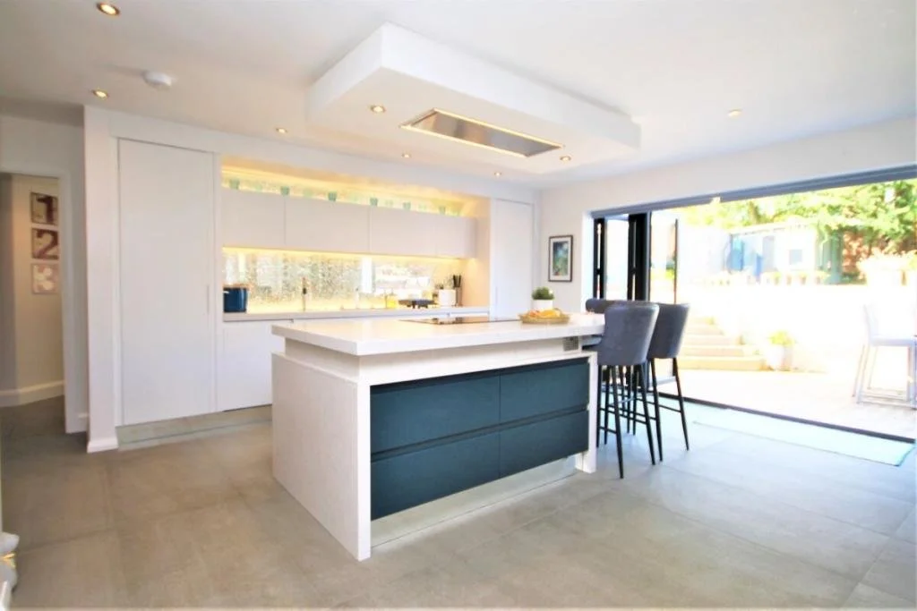Modern kitchen with white cabinets, a kitchen island with dark drawers, gray bar stools, and large sliding glass doors leading outside.