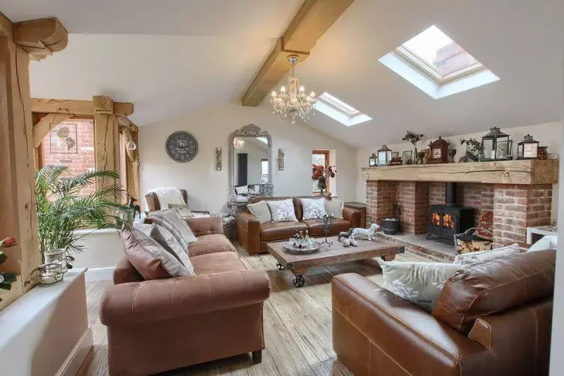 Living room with leather and upholstered sofas, a brick fireplace with a wood-burning stove, a wooden coffee table, and skylights in the ceiling, decorated with plants, lanterns, and vintage decor.