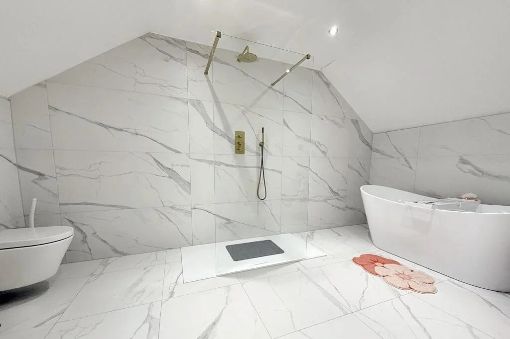 Modern bathroom with marble walls and floors, a glass-enclosed shower with gold fixtures, a freestanding bathtub, and a toilet.