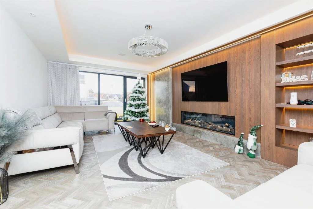 Modern living room with a Christmas tree, white sofas, wooden accent wall with a mounted TV, electric fireplace, and holiday decorations.