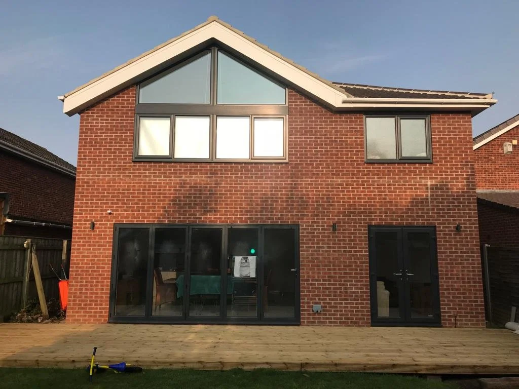 Back of a two-story brick house with large glass sliding doors on the ground floor and multiple windows on the second floor, with a wooden deck in the yard.