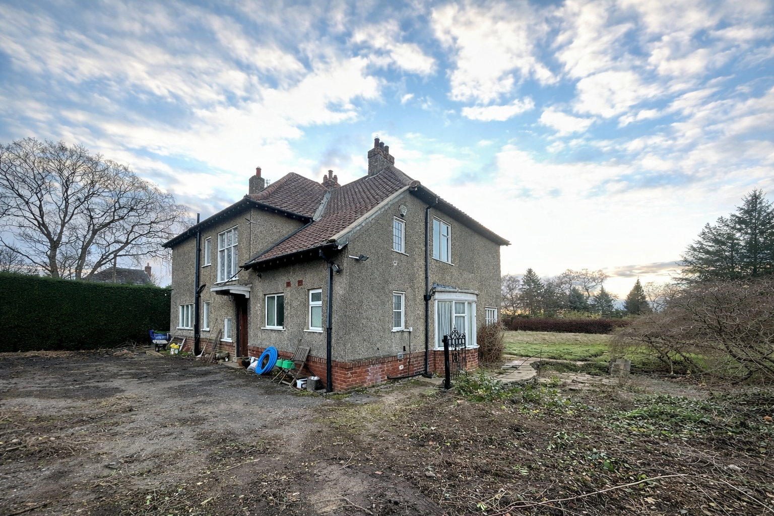 A quiet house with a backyard, overcast sky, and a mix of bare and leafy trees.