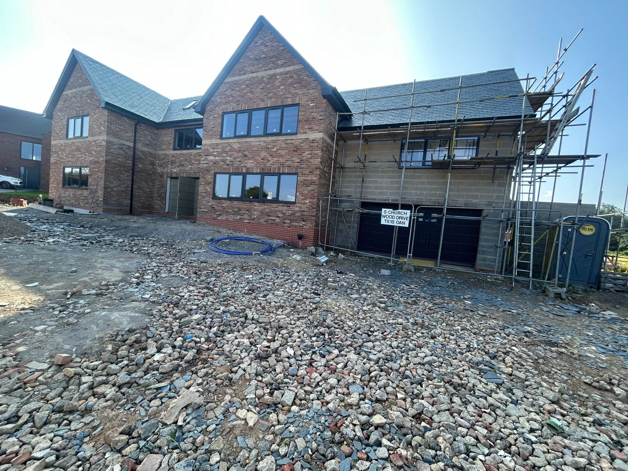 Newly constructed brick house under construction with scaffolding, gravel front yard, and construction signs.