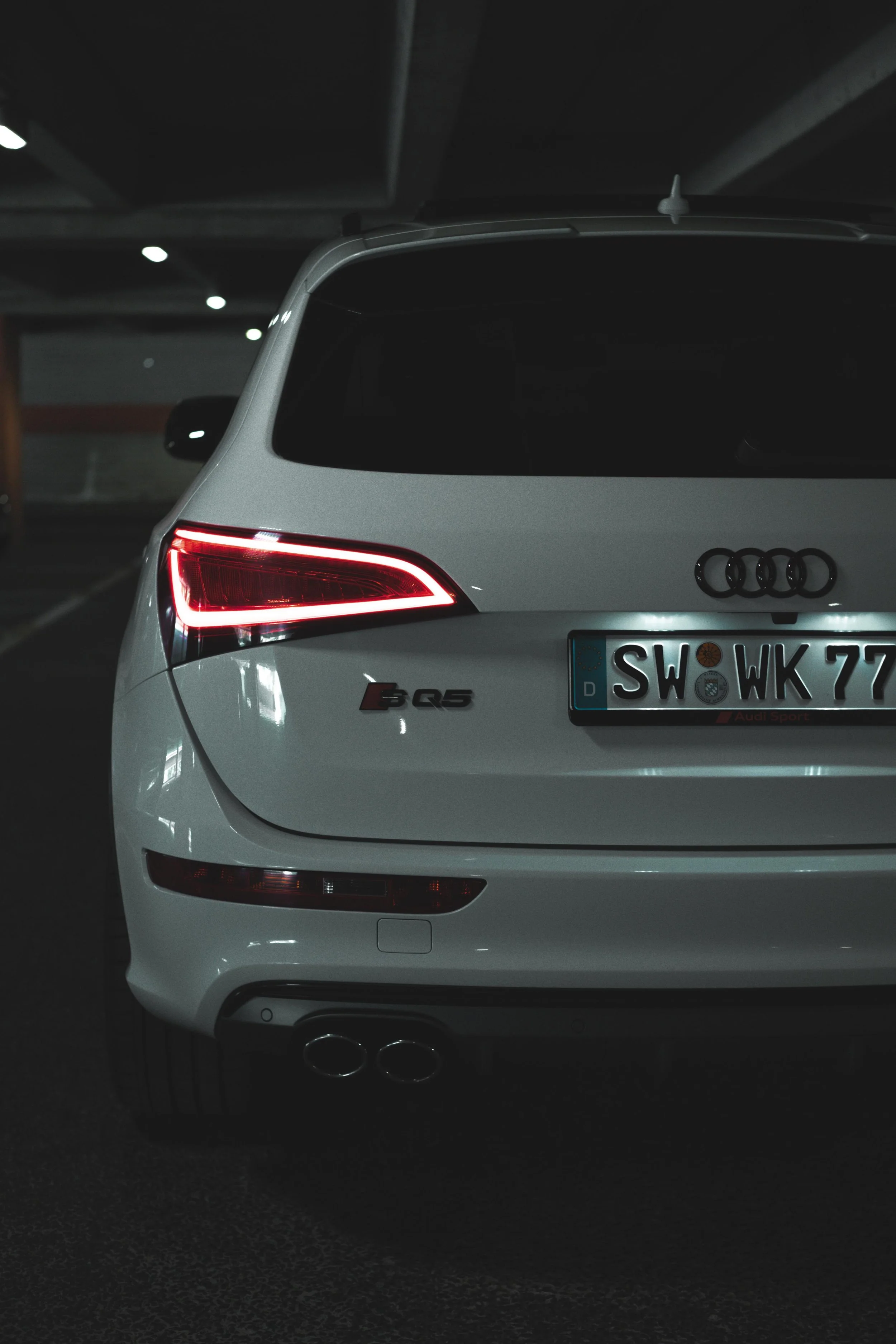Weißer Audi SQ5 mit schwarzem Hintergrund, Rückansicht, in einer Tiefgarage, mit Blick auf das hintere Ende und die Rücklichter.