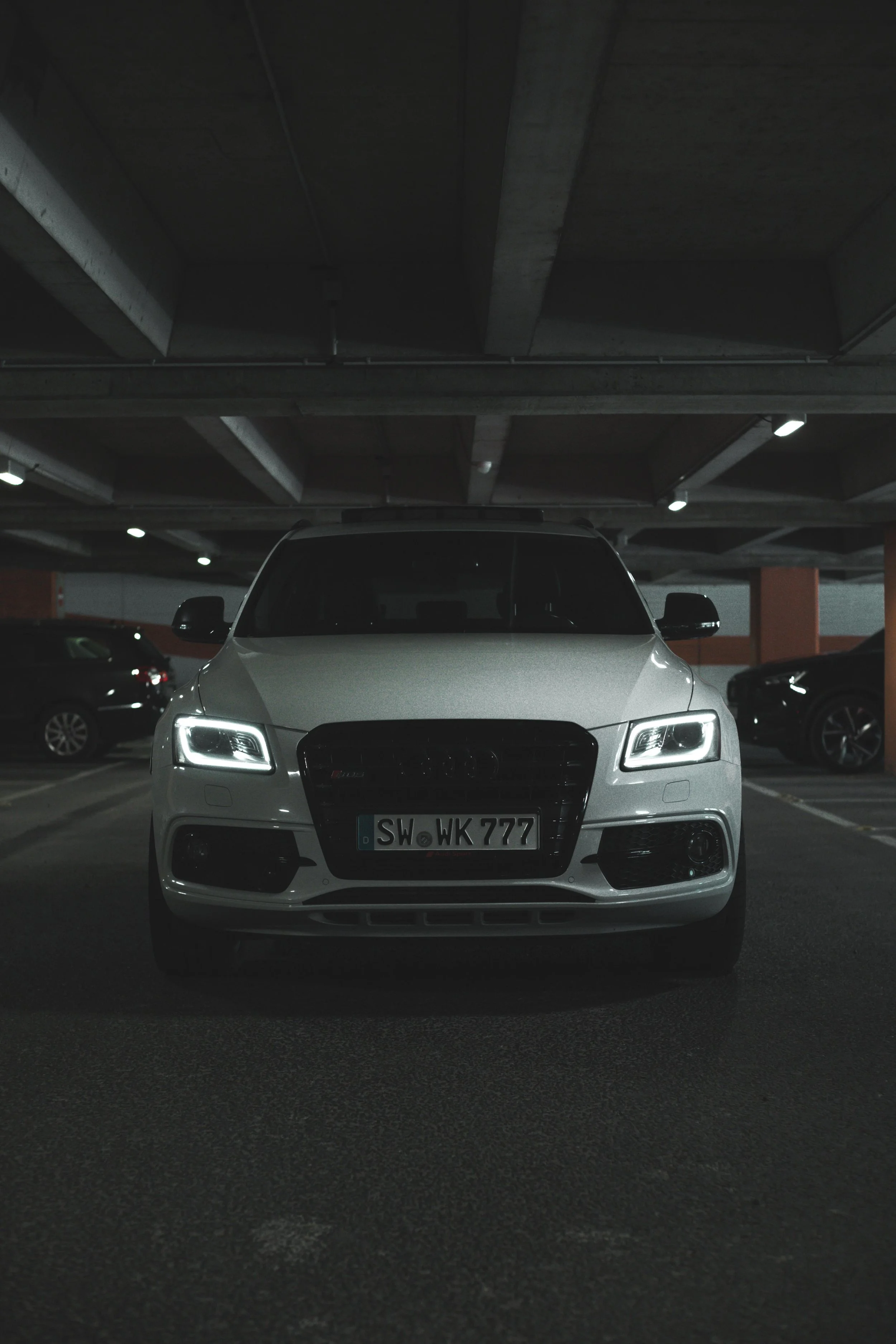 Ein weißer Audi SQ5 SUV in einer Tiefgarage mit dunklem Decke und mehreren anderen geparkten Fahrzeugen